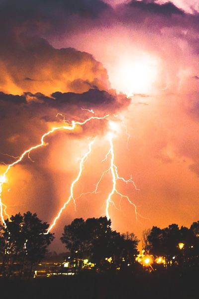 Bild eines Unwetters mit Blitzen, die in eine Baumgruppe einschlagen.
