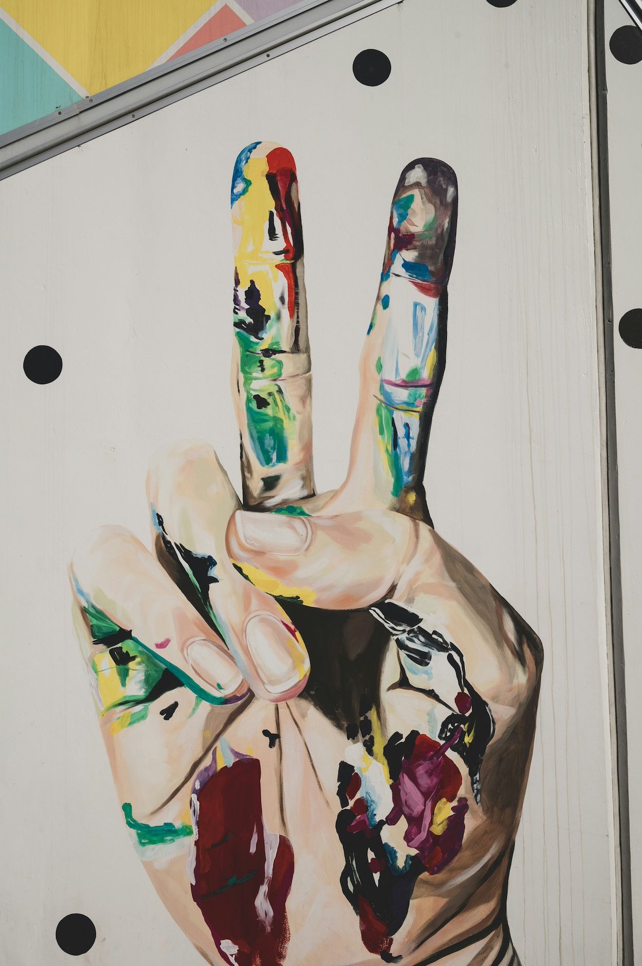 Kunstwerk an einer Wand, darauf zu sehen ist eine bunte Hand, die das Peace-Zeichen macht.